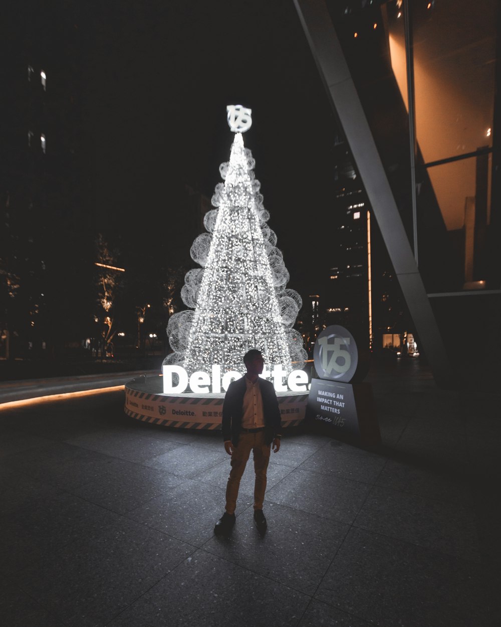 mulher na jaqueta preta de pé perto da árvore de Natal iluminada durante a noite