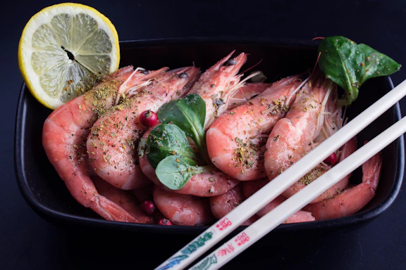 Close-up of a golden crispy shrimp roll garnished with fresh ginger and herbs on a sleek black plate.
