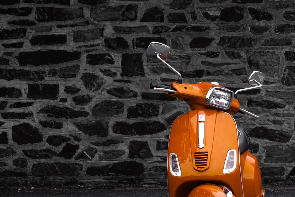orange motor scooter parked beside black and white wall