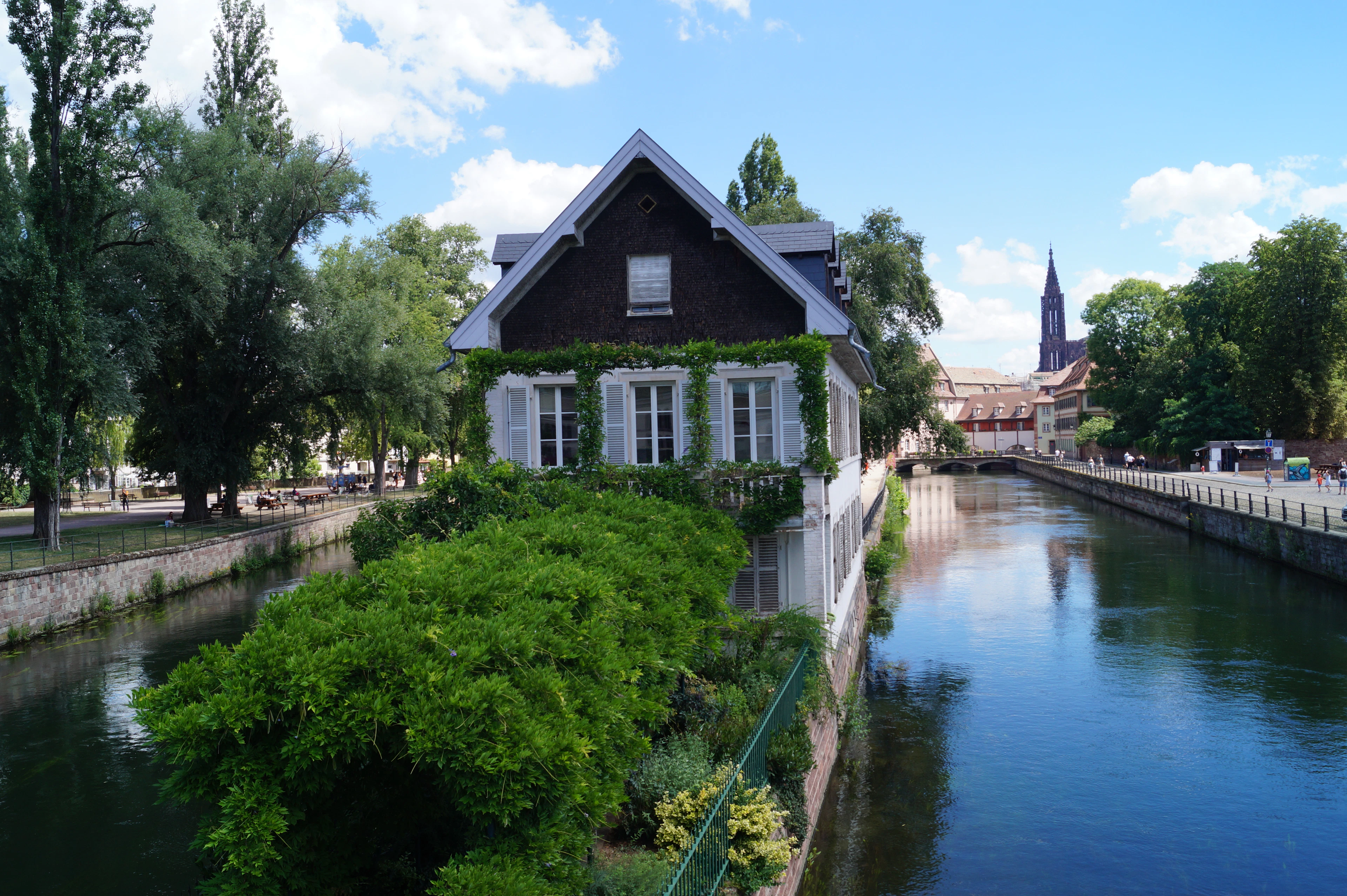 A small gabled house on a canal island in La Petite France, with Strasbourg Cathedral's spire rising behind it.