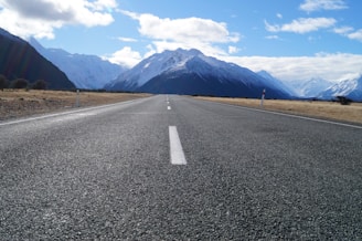 gray asphalt road near mountain range under blue sky during daytime