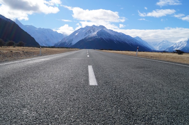 gray asphalt road near mountain range under blue sky during daytime