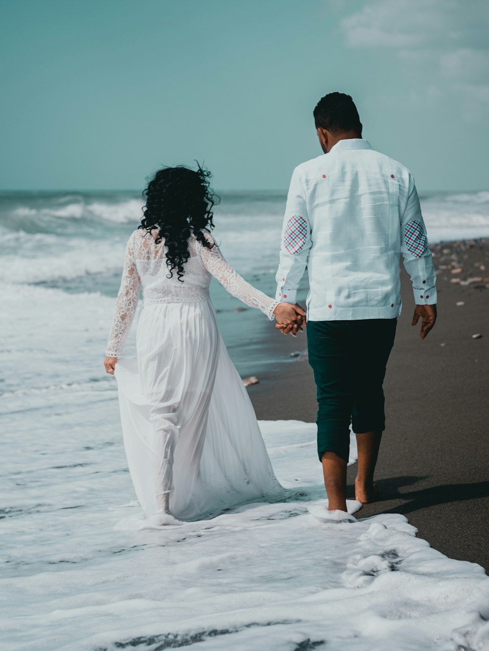 man and woman holding hands while walking on beach during daytime