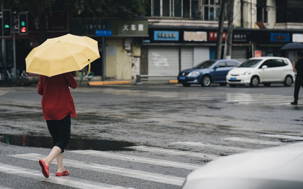 mulher no casaco vermelho que segura o guarda-chuva amarelo andando na rua durante o dia