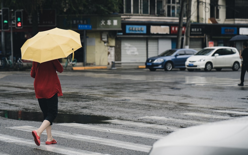 woman in red coat holding yellow umbrella walking on street during daytime