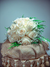 A lush bridal bouquet of deep emerald greens and soft cream roses accented with gold ribbons.
