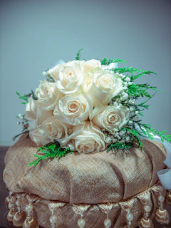 A lush bridal bouquet featuring deep emerald greens and soft cream roses tied with a gold ribbon.