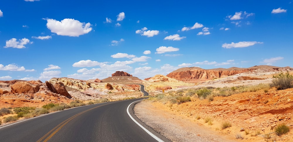 gray asphalt road between brown mountains under blue sky during daytime