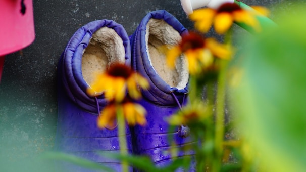 A pair of waterproof gardening boots placed beside a flower bed.