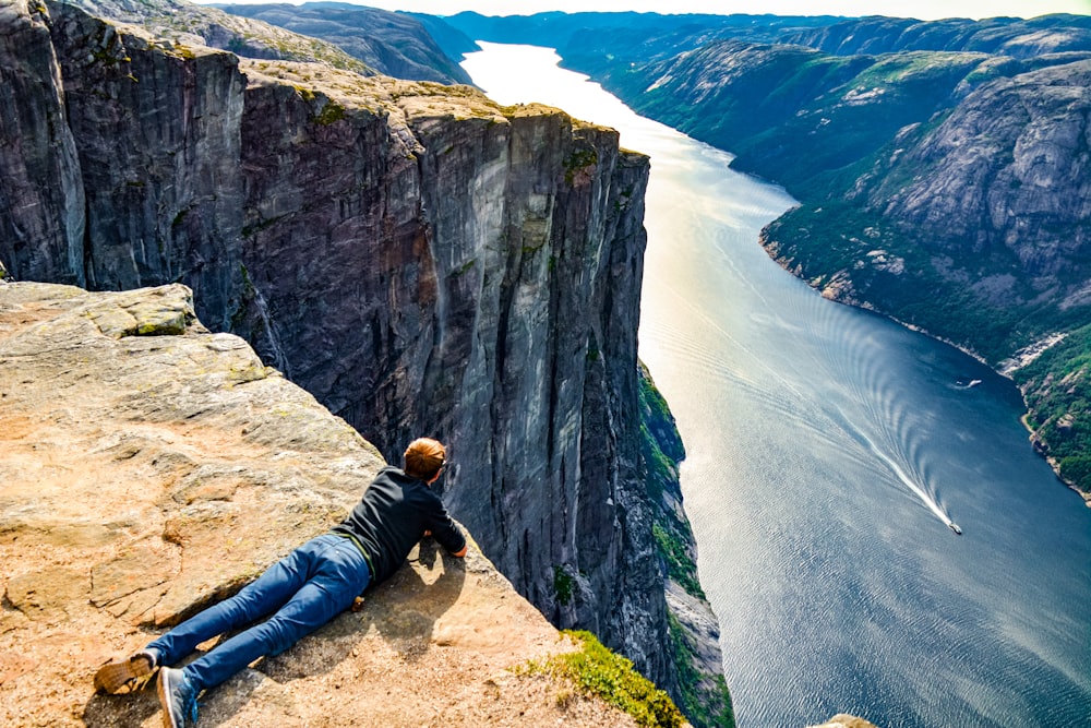 man in black jacket lying on brown rock formation near body of water during daytime