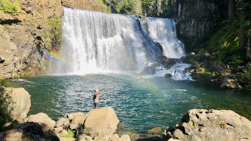 woman in black tank top standing on rock near waterfalls during daytime