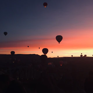 Sunset view from a hot air balloon with silhouettes of other balloons in the distance
