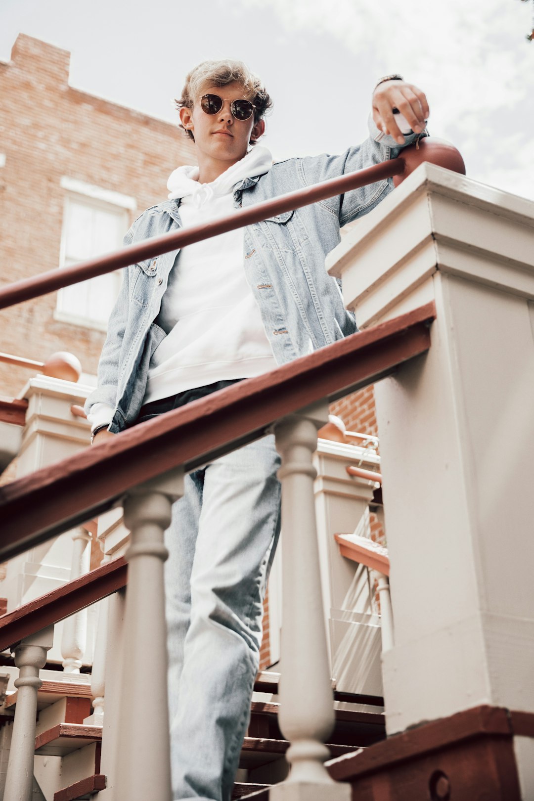 woman in white long sleeve shirt and blue denim jeans standing on brown wooden staircase