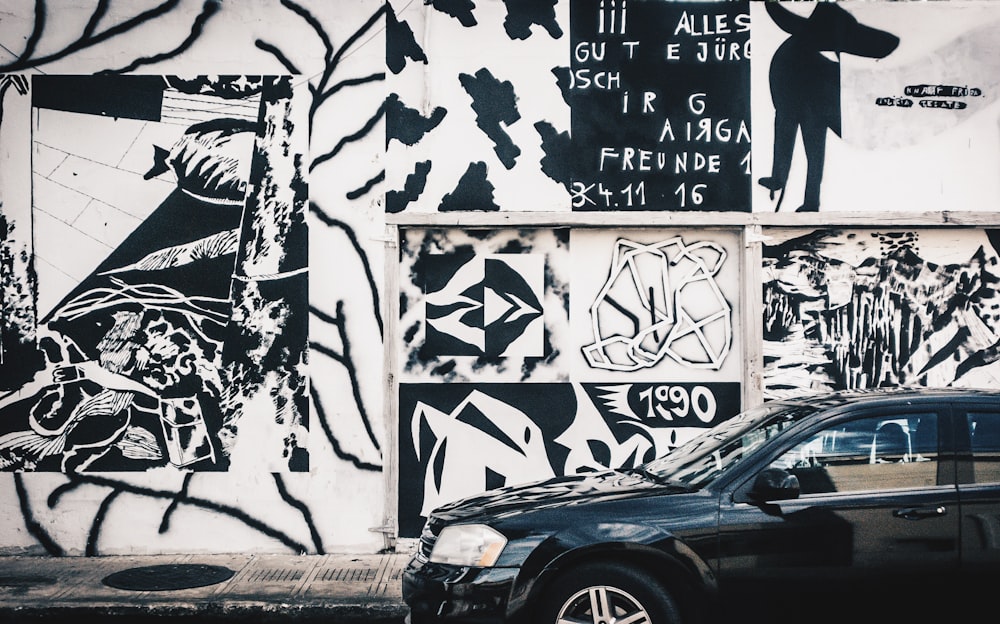 black car parked beside white wall with graffiti