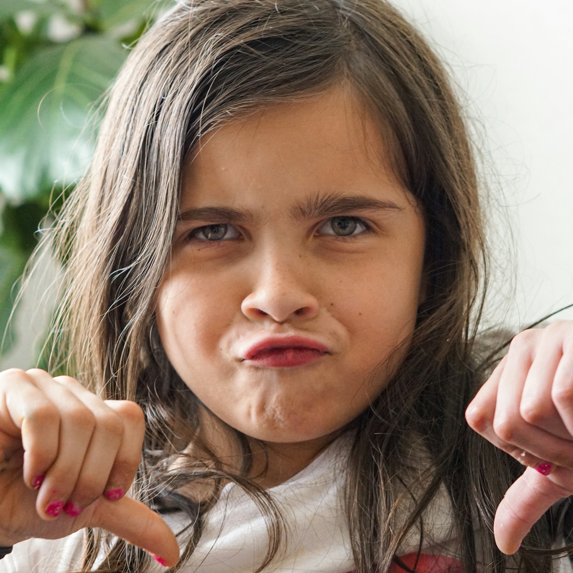 Pretty young girl making a disapproving face while giving the thumbs down about not going back to school.