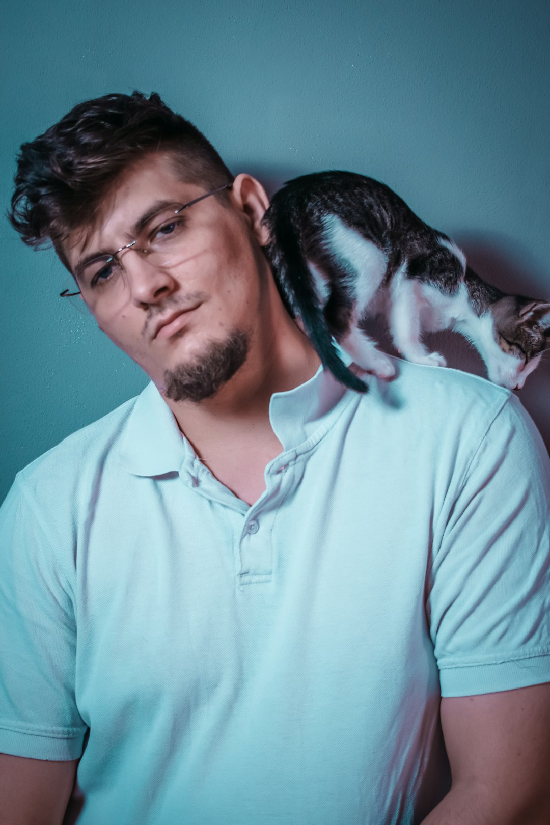 man in teal polo shirt holding black and white cat