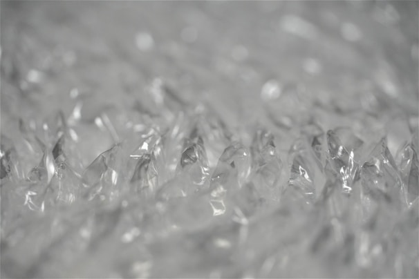 Close-up view of clear bubble wrap showing its texture and translucent material. The bubbles appear as inflated, individual pockets that reflect light. The image captures the minute details of the bubble wrap, giving a sense of its soft and protective quality.