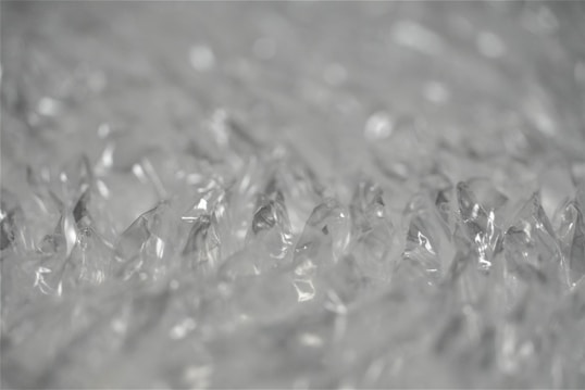 Close-up view of clear bubble wrap showing its texture and translucent material. The bubbles appear as inflated, individual pockets that reflect light. The image captures the minute details of the bubble wrap, giving a sense of its soft and protective quality.