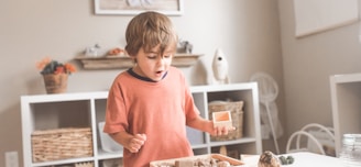 boy in orange crew neck t-shirt standing in front of white wooden table with cupcakes