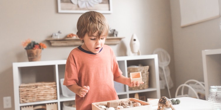 boy in orange crew neck t-shirt standing in front of white wooden table with cupcakes