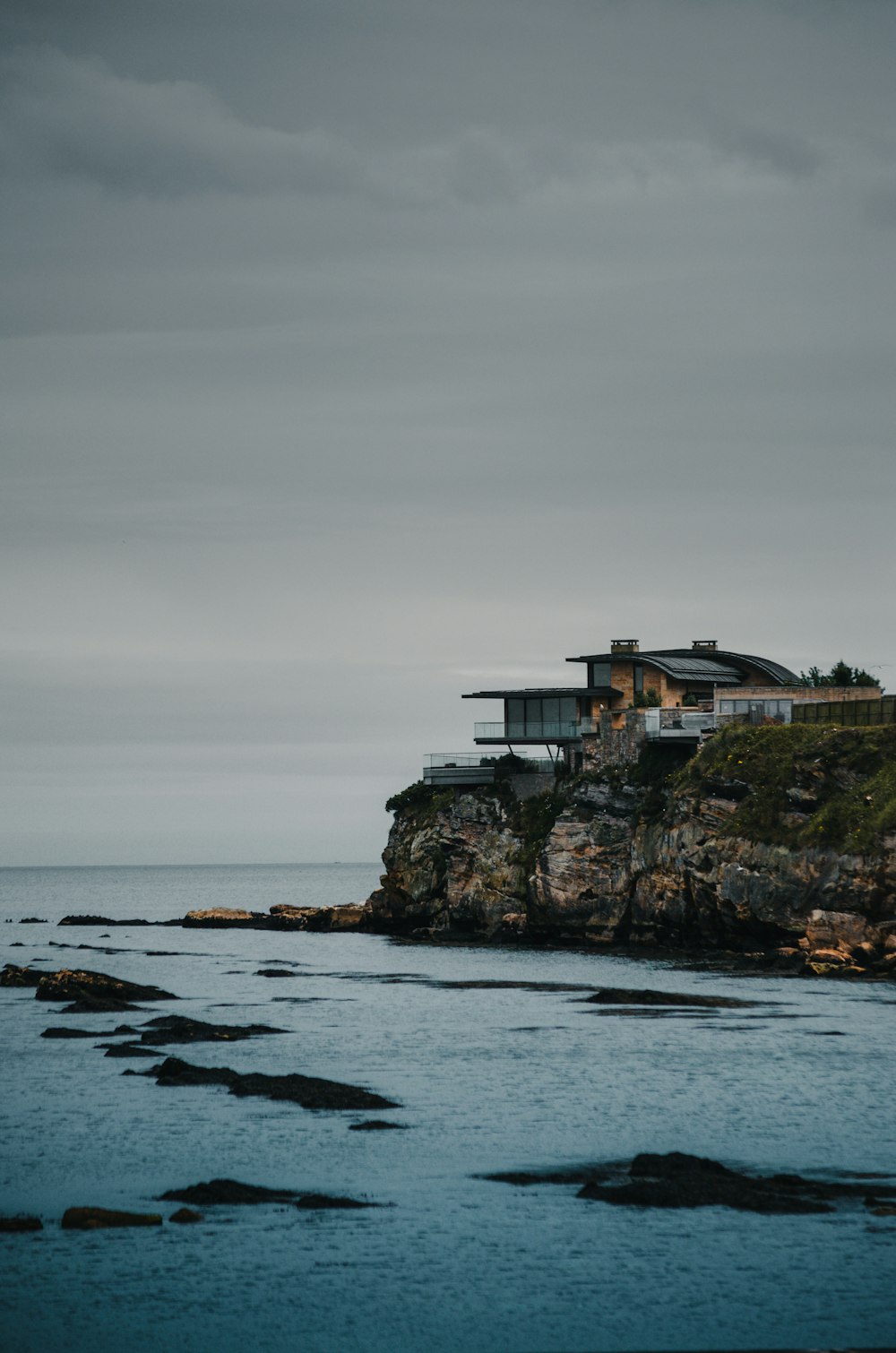 white and brown house on top of the hill by the sea under grey cloudy sky