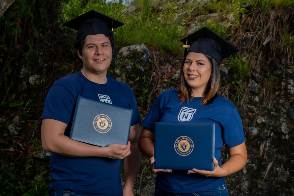 man in blue crew neck t-shirt standing beside woman in black academic dress