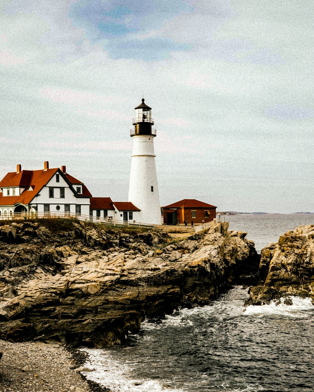 white and brown lighthouse on brown rock formation near body of water during daytime