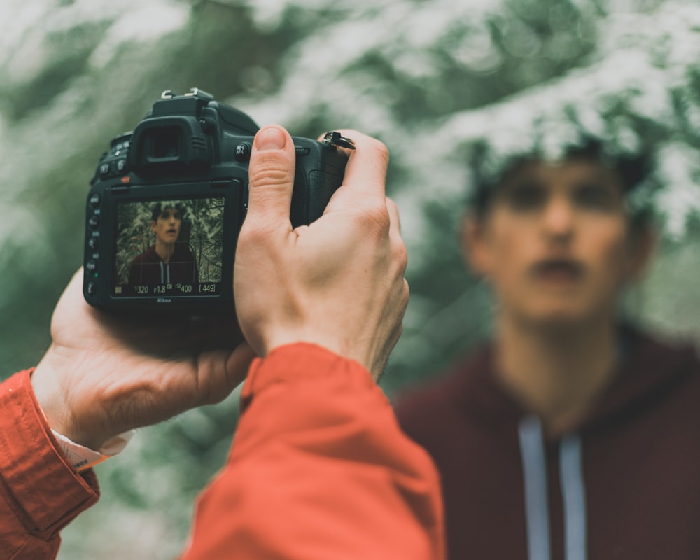 Hombre con chaqueta naranja sosteniendo una cámara DSLR negra