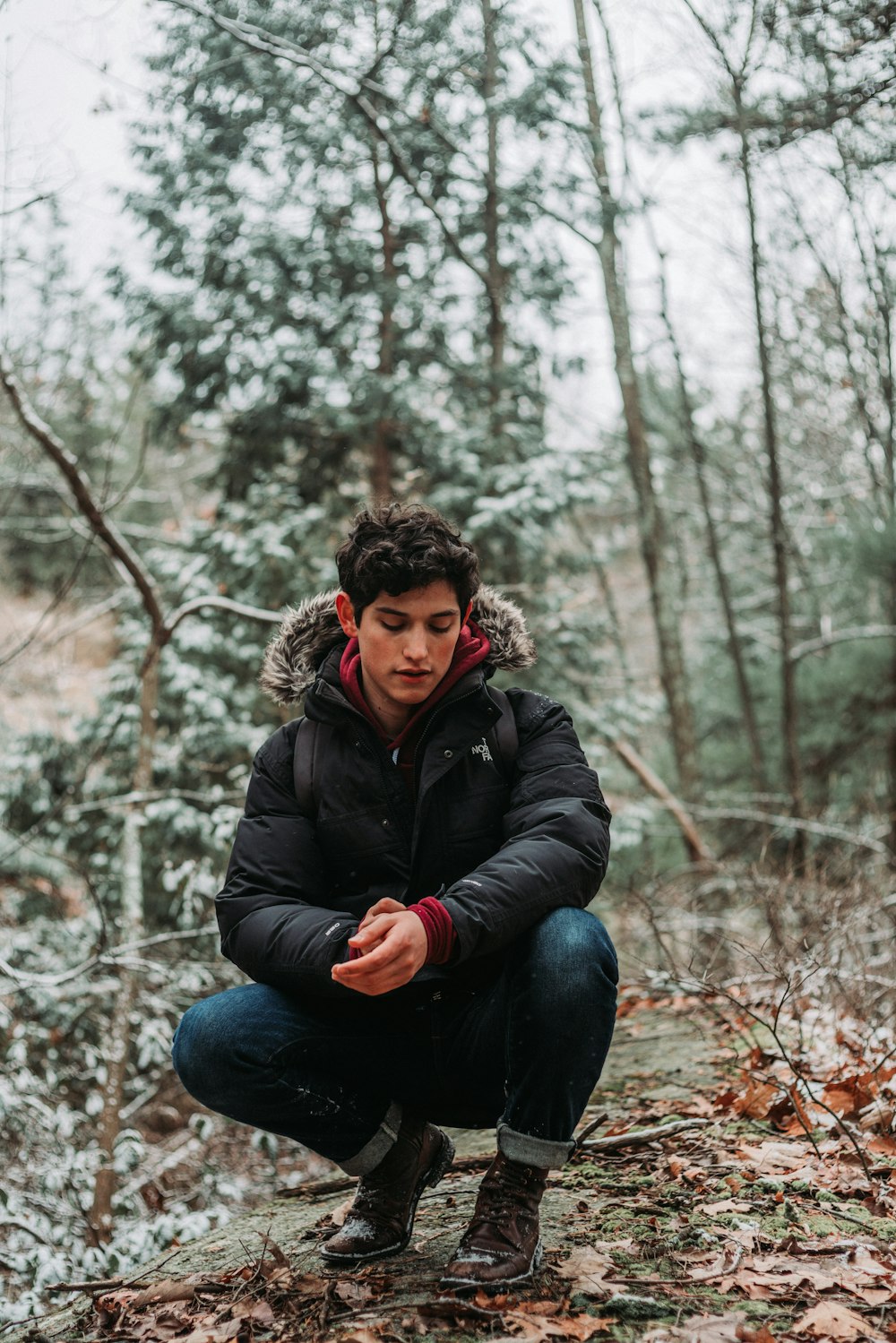 woman in black jacket and blue denim jeans sitting on rock