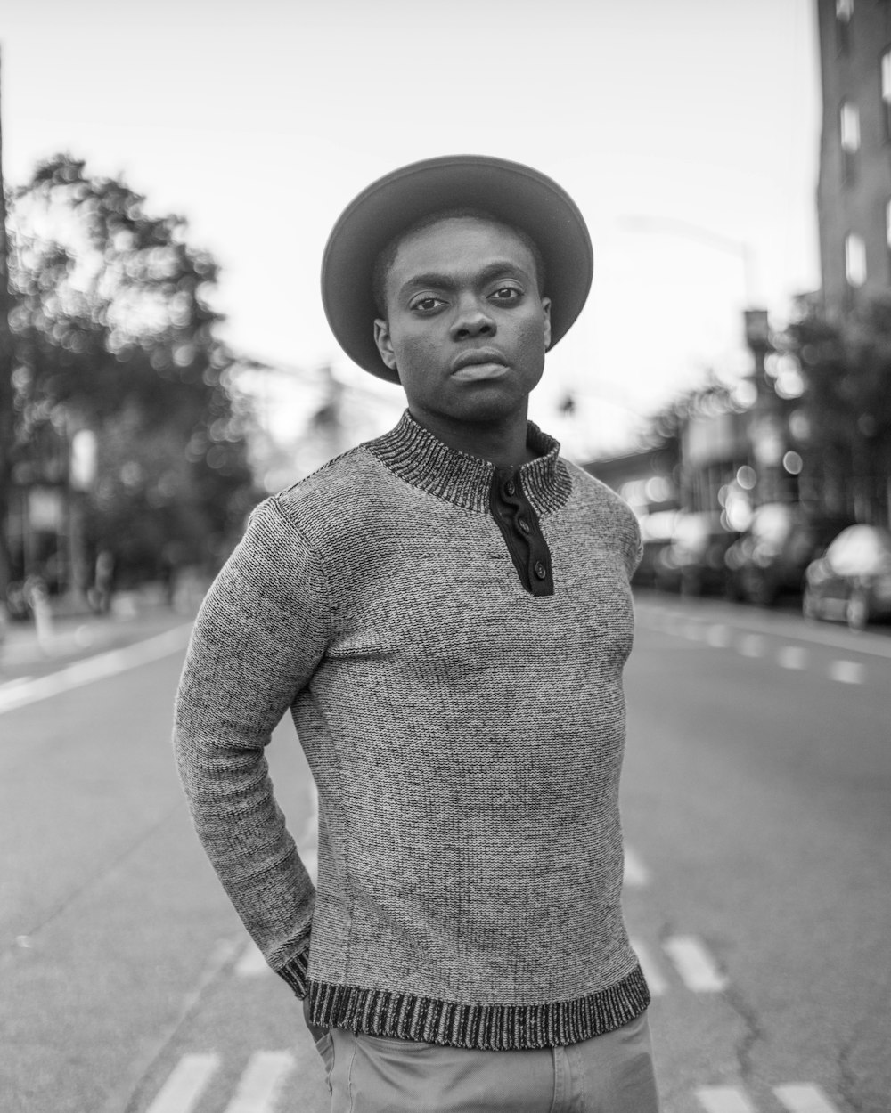 grayscale photo of man in sweater and hat standing on road