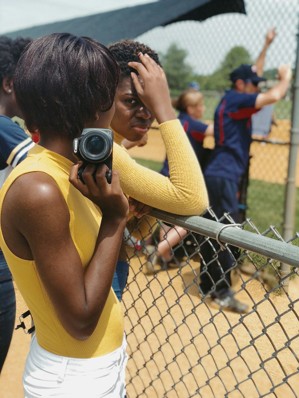 femme en débardeur jaune tenant un appareil photo reflex numérique noir