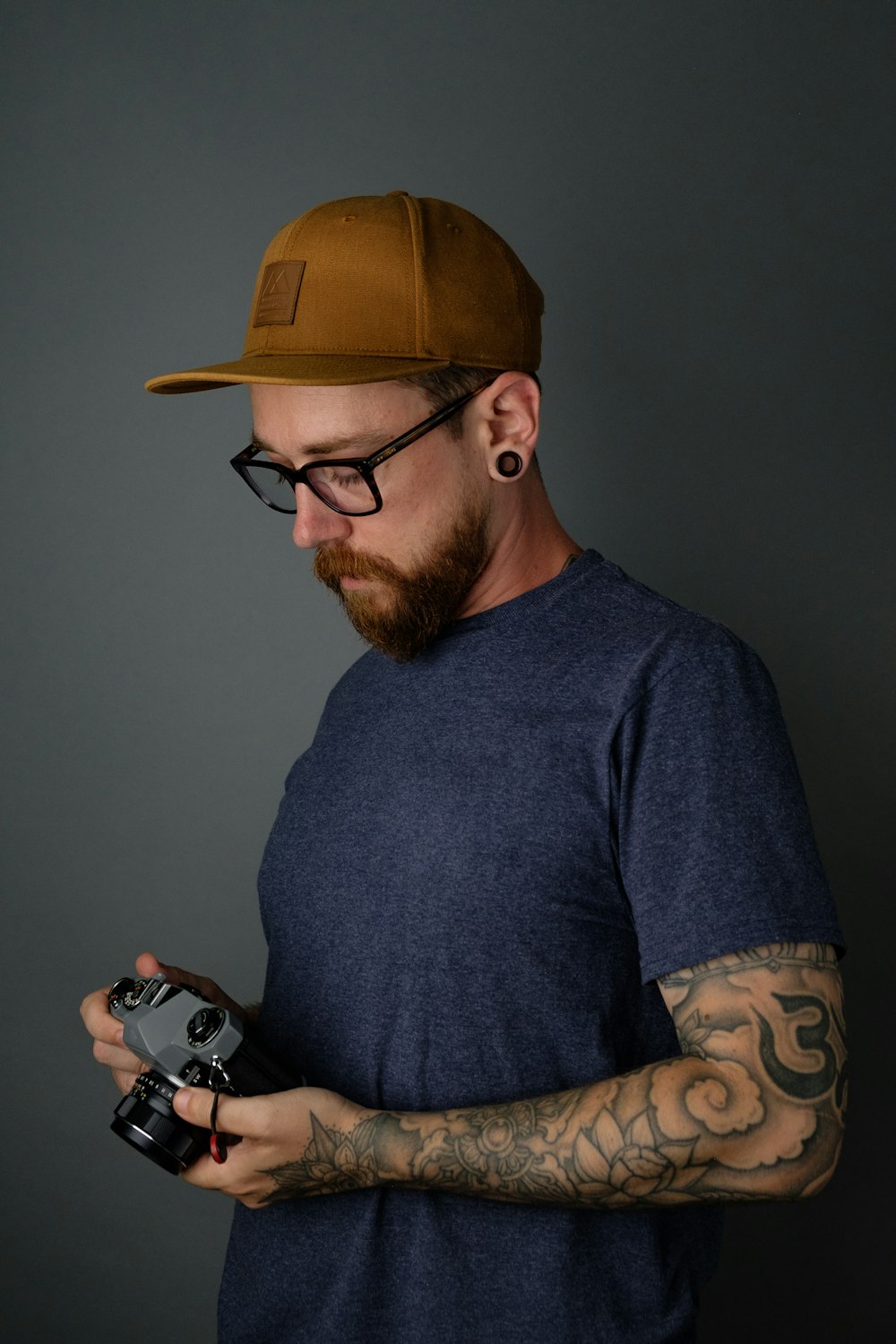 man in blue crew neck shirt wearing brown cap holding black and silver dslr camera