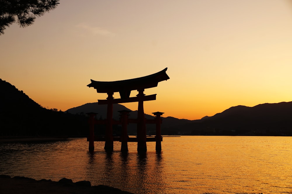 silhouette of gazebo near body of water during sunset