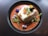 A beautifully plated dish featuring a rectangular piece of white fish garnished with fried garlic slices, microgreens, and edible flowers. The fish is surrounded by a bright orange puree or sauce, adding a contrasting color to the composition.