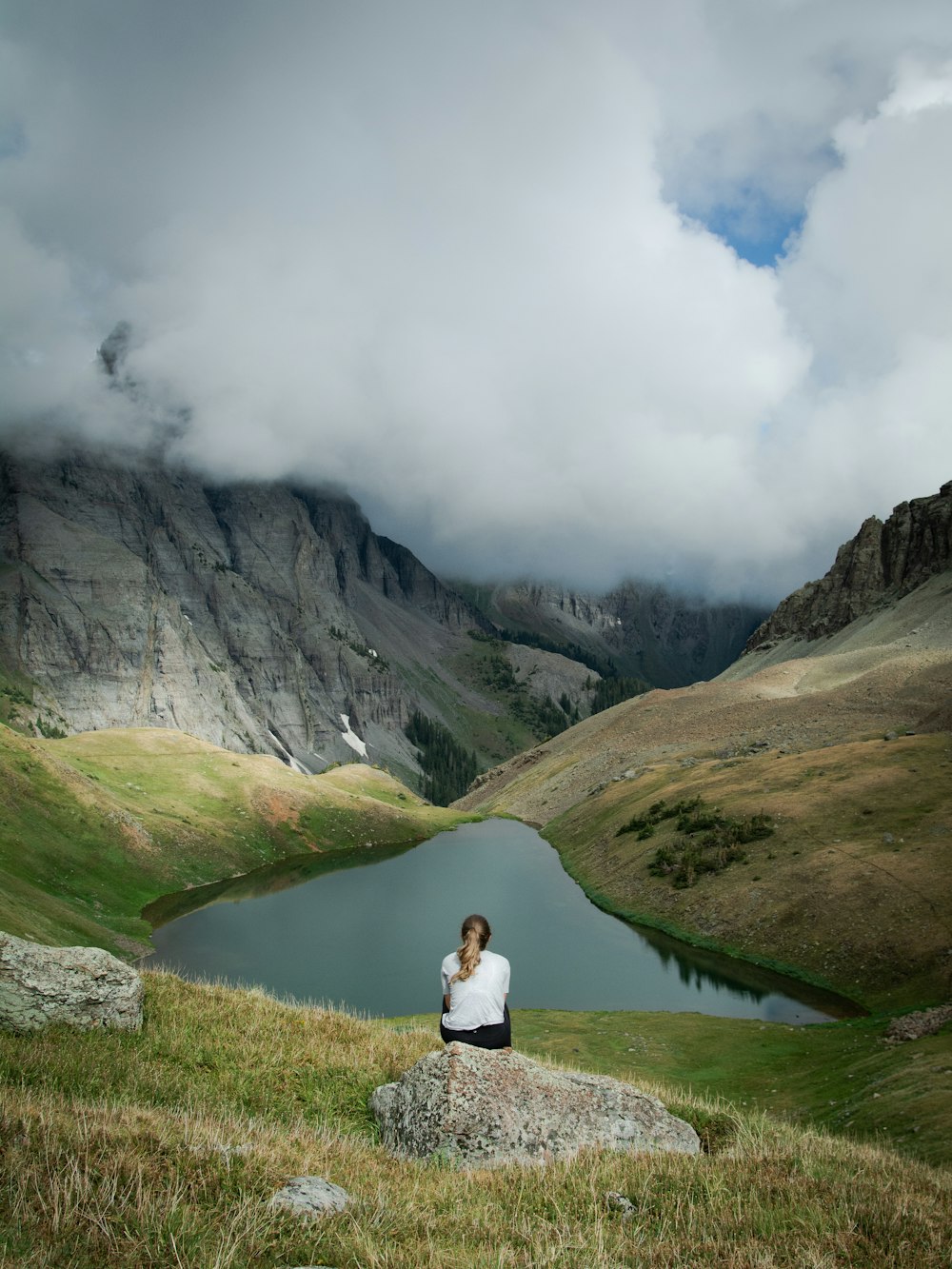 person in white jacket sitting on green grass field near gray mountain during daytime