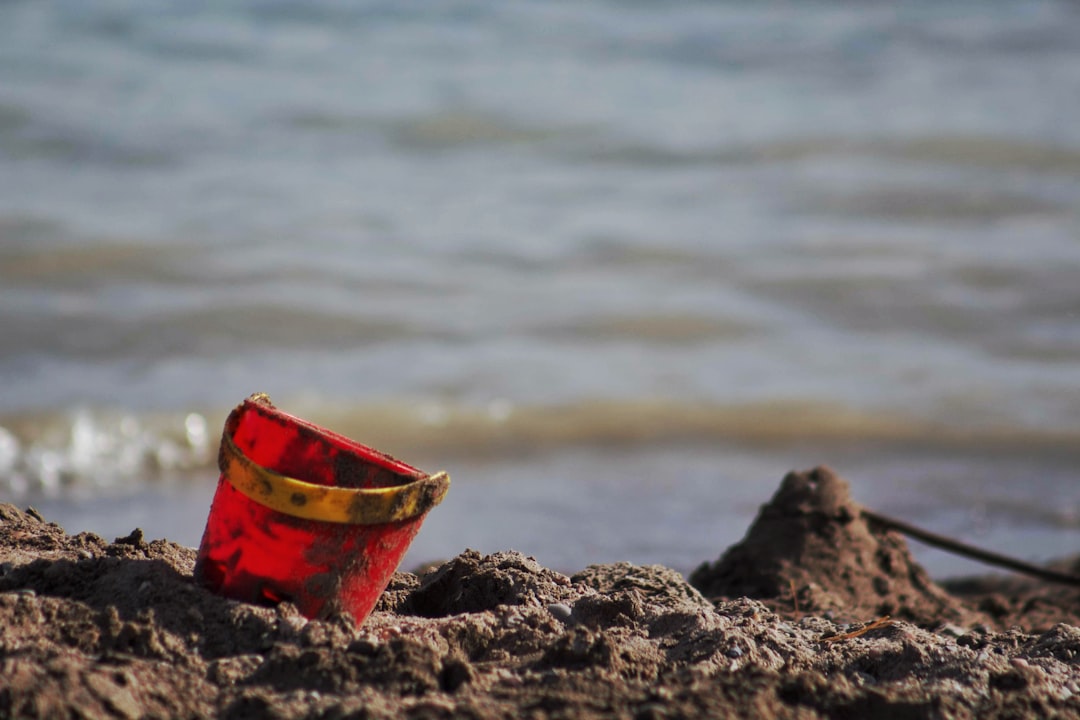 red plastic bucket on brown sand near body of water during daytime