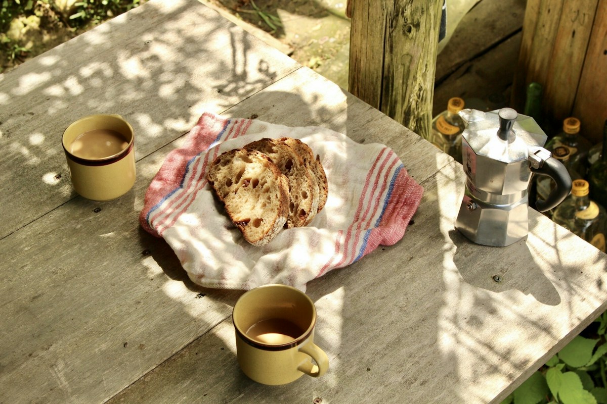A loaf of bread on a plate next to a mug, ideal for sports team potluck ideas or tailgate potluck gatherings.
