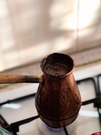 Elegant copper coffee pot steaming beside a cream-colored ceramic cup on a dark brown wooden table.