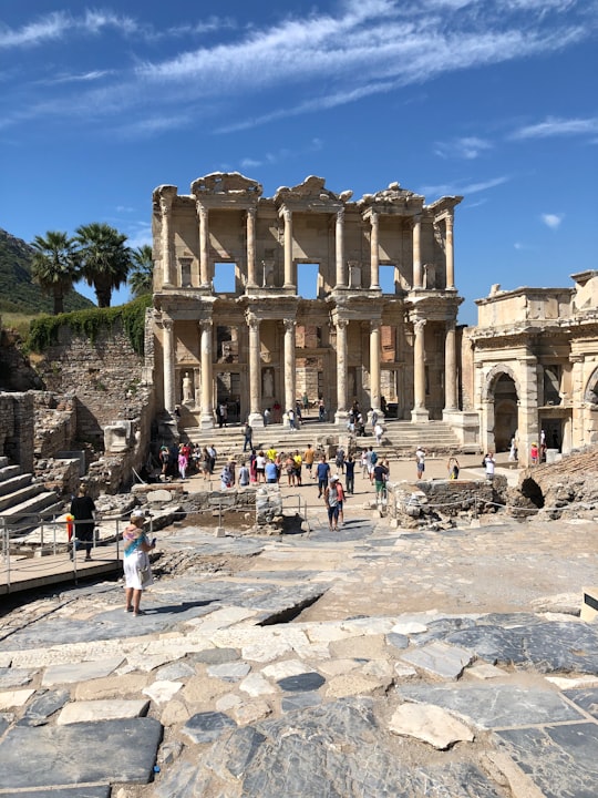 people walking on gray concrete pathway near beige concrete building during daytime in Library of Celsus Turkey
