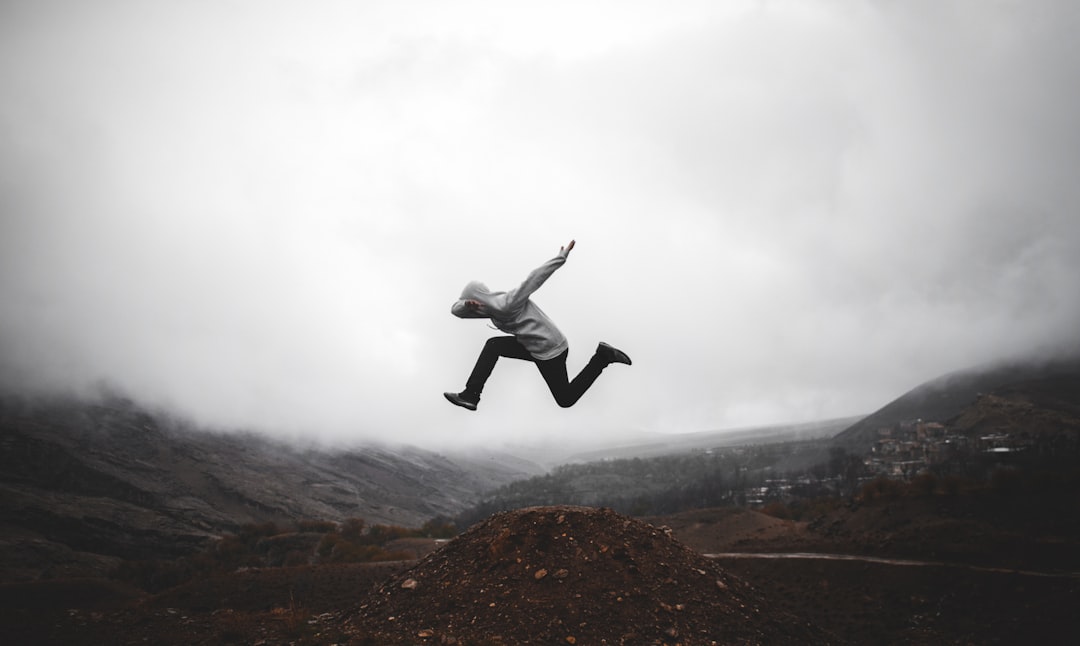 man in black jacket and pants jumping on brown rock formation during daytime, somewhere in the sky