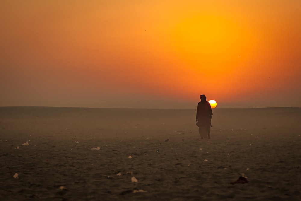 Hombre en sudadera con capucha amarilla de pie en la playa durante la puesta del sol