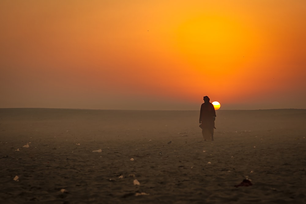 man in yellow hoodie standing on beach during sunset