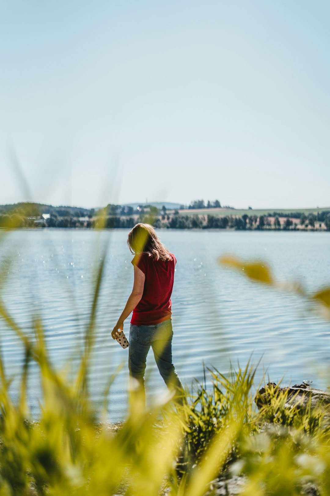 woman in red tank top and black pants standing on green grass near body of water