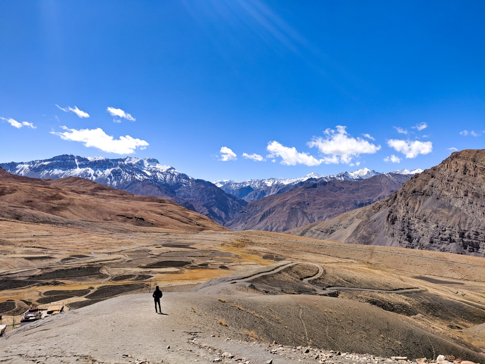 person walking on dirt road near brown mountains under blue sky during daytime