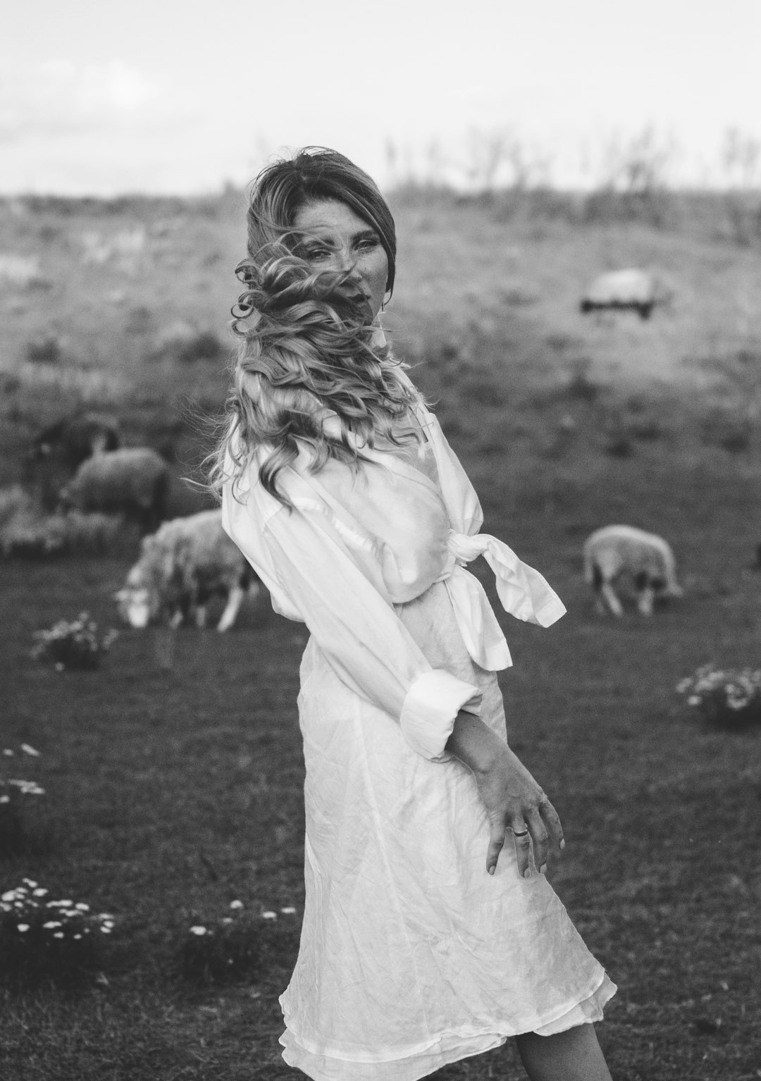 grayscale photo of woman in white dress standing on grass field