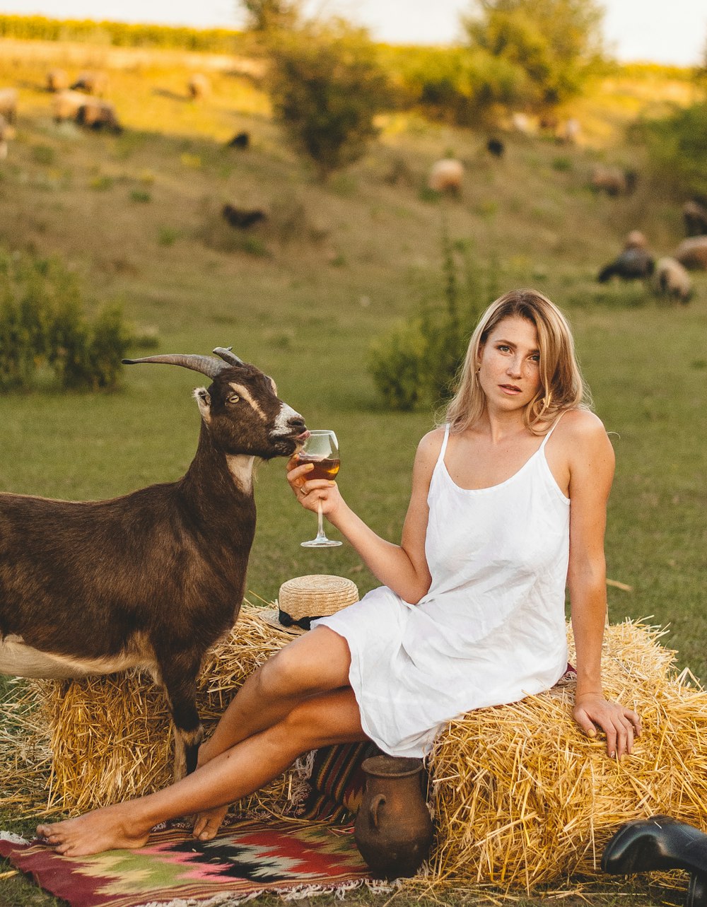 woman in white tank top sitting on brown hay with black and white goat