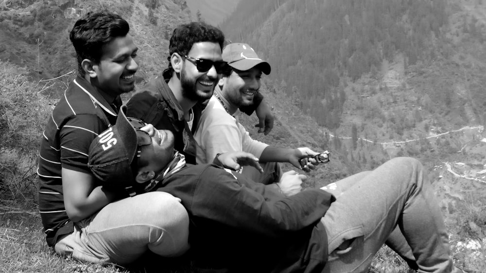 grayscale photo of 3 men sitting on rock