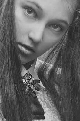 A dark, moody portrait of a figure cloaked in black lace with sharp silver accessories.