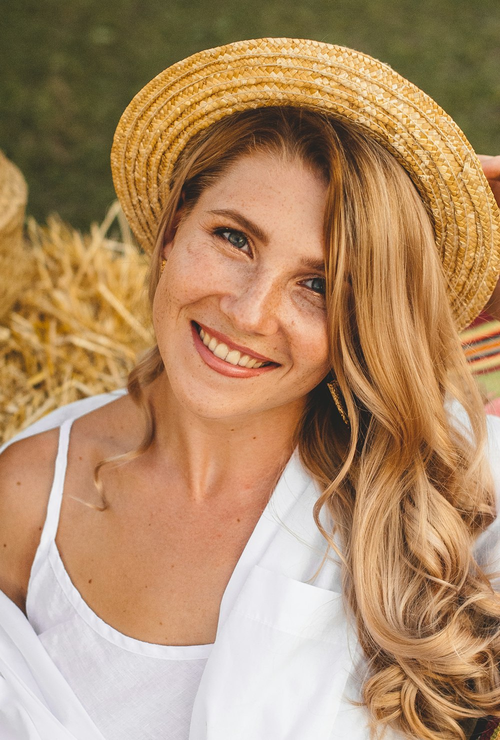 smiling woman in white tank top wearing brown straw hat