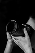 grayscale photo of person holding nikon dslr camera